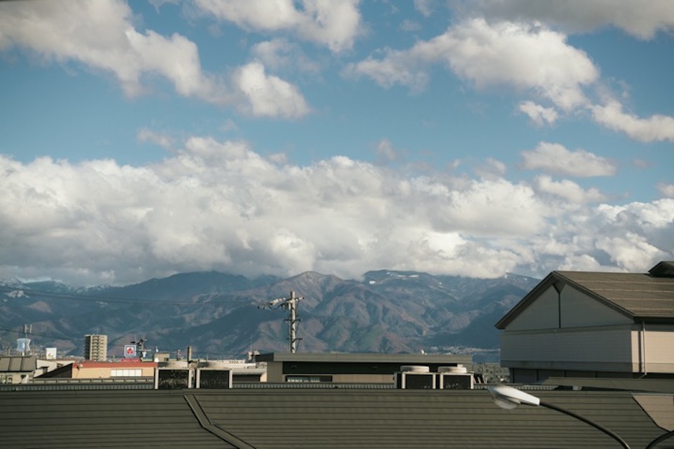 窓から見える、小布施、須坂方面に見える山並み。ここの標高の高さがうかがえる。雨上がりの朝だったから、空にはまだ大きな雲がとどまっていた。