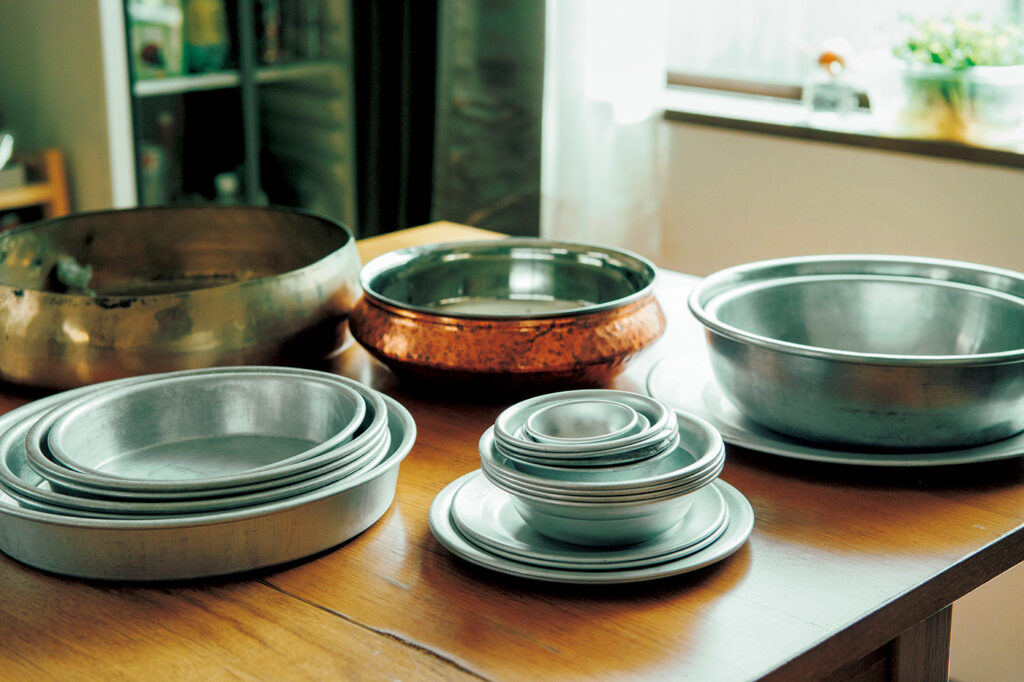 手前のアルミ皿はみな出自が違う。右は台湾、中央はインド、左はマレーシア。奥の銅製カレー皿はインドから。左奥は韓国の骨董市で、ふきんの入れ物にするため持ち帰ったのだが、おそらく楽器の”銅鑼”だと思われる。