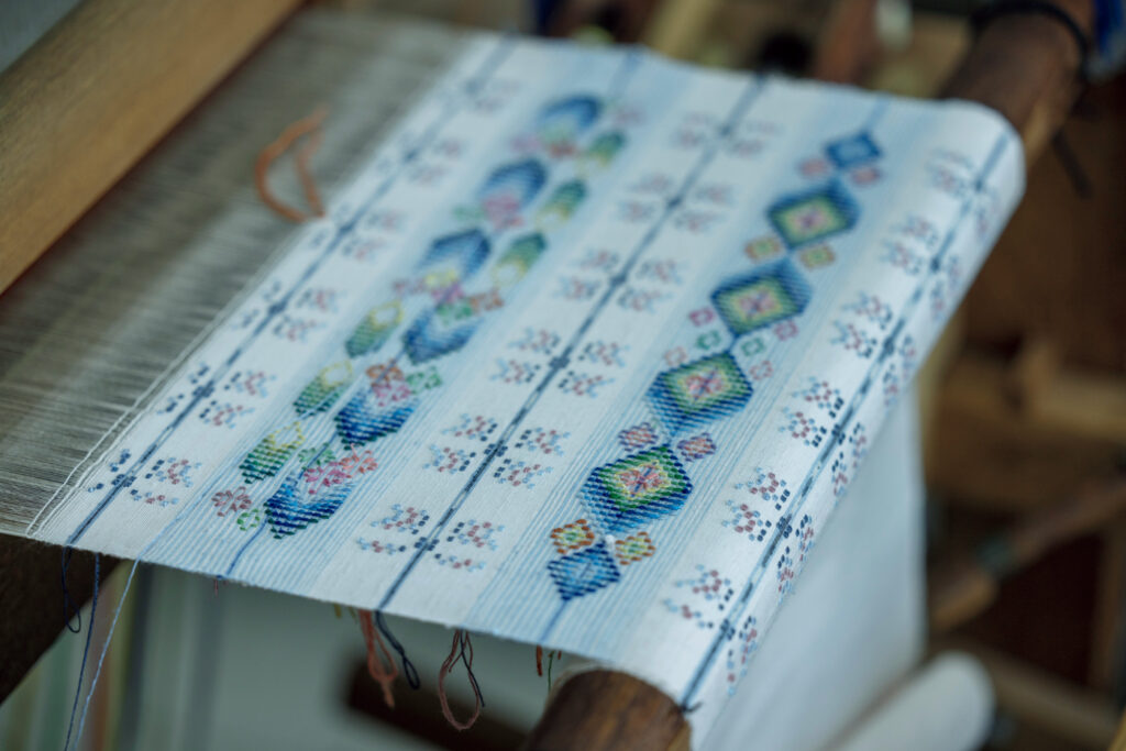 沖縄産植物などを使って糸を染め、花モチーフの柄を組み合わせながら様々な紋様を織り上げる読谷山花織（ゆんたんざはなうい）。読谷村伝統工芸センターで織物を体験するプランも。