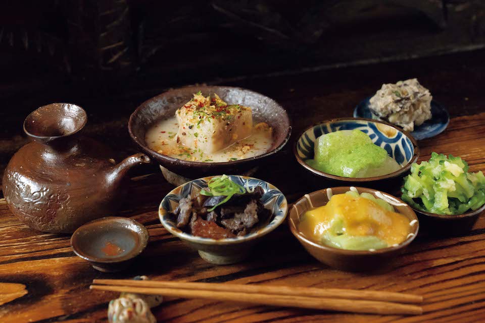 店主手製の『オニノウデ』の琉球伝統料理。塩ラフテー、島ニンジンの味噌煮、ドゥルワカシーなど、いずれも泡盛に合う味に。酒器は名匠・國吉清尚（くによし・せいしょう）の作品。