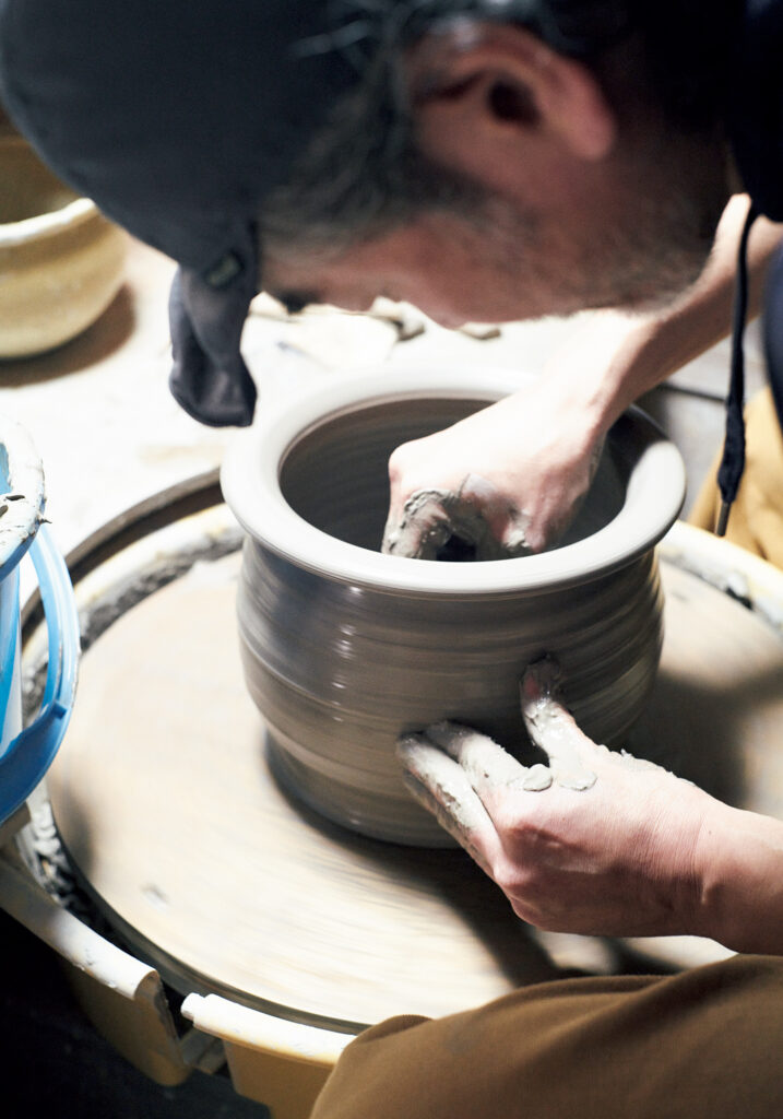 『やまほん陶房』にて作陶する忠正さん。大学で木彫を専攻したのち、陶芸の道へ進んだ。自身の作品は土鍋などの土ものに加えて、型物で作る半磁器の匙なども。