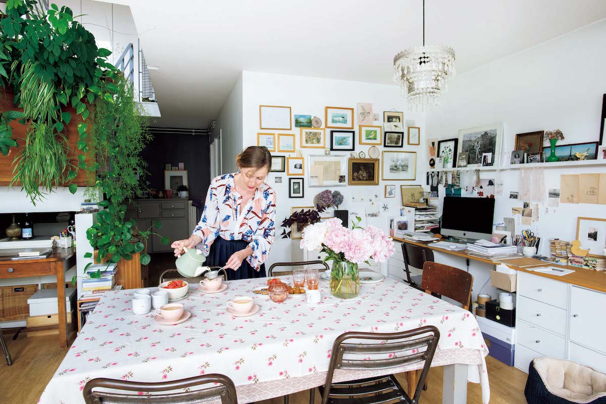 お茶の用意をするシビル。食器はすべてアンティーク。テーブルクロスは大好きな花柄。テーブルの上には満開の芍薬を、階段の踊り場にはベゴニアなどグリーンを飾っている。右はワークスペース。 お茶の用意をするシビル。食器はすべてアンティーク。テーブルクロスは大好きな花柄。テーブルの上には満開の芍薬を、階段の踊り場にはベゴニアなどグリーンを飾っている。右はワークスペース。