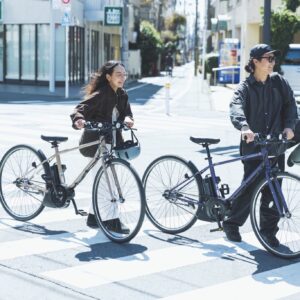 街中を散策する鈴木竜也さん、鈴木茜さん夫妻。〈ヤマハ発動機〉の電動アシスト自転車PAS CRAIGは、景色に溶け込むシンプルなデザイン。竜也さんはシックでモダンなマットラベンダー、茜さんはやわらかく知的な印象のマットグレイッシュベージュをチョイス。