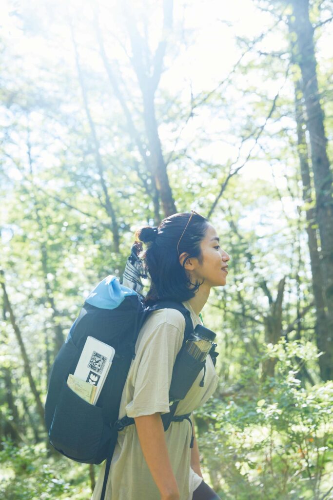 気持ちのいい木漏れ日が差す樹林帯。愛用するのは〈アイスブレーカー〉のメリノウールTシャツ。「山でのインナーやベースレイヤーには、メリノウール一択です」山に登り、本来の自分を取り戻す。フリーランスPR・佐竹彩さんのひとりの時間のつくり方、楽しみ方。