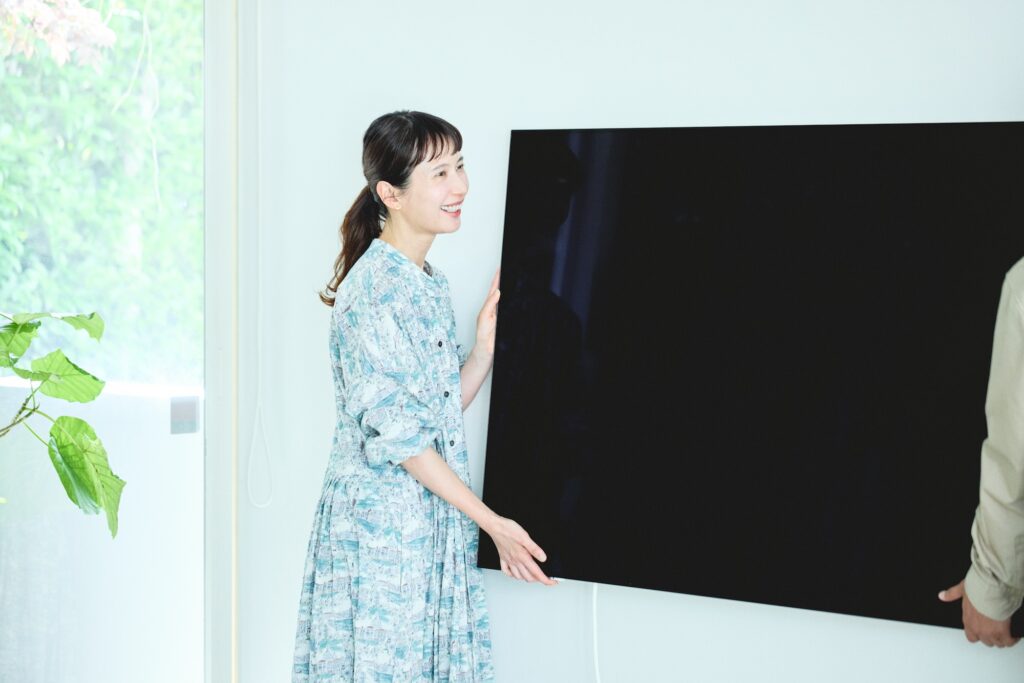 石こうボードの壁への取り付けは簡単。65Vのモニターの重量は約15.5kgで、大人2人でラクに持ちあげられる軽さ。壁に付けた専用金具 (フック金具) に引っ掛けるだけで、設置は完了。「下部の専用金具 (フック金具) はマグネットになっているので、取り外しもしやすいですね」