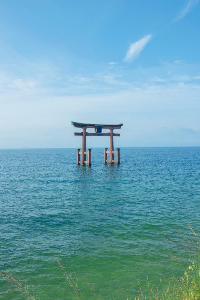 滋賀・奥琵琶湖で聖なる水辺を歩く旅。前編 | 近江最古の大社『白鬚神社』の湖中大鳥居。創建2000年余。『白鬚神社』(高島市鵜川215)は延命長寿のほか、縁結びや子授け、福徳開運、攘災招福、商売繁盛、交通安全など、人の世のあらゆる導きおよび道開きの神として信仰されてきた。湖中大鳥居は古より波打ち際に見え隠れしていた、また天下異変の前兆に突如姿を現したといった伝説が残り、室町時代の屏風絵にも描かれている。実際に鳥居が建立されたのは1937年、現鳥居は1981年に建て替えられたもの。 滋賀・奥琵琶湖で聖なる水辺を歩く旅。前編