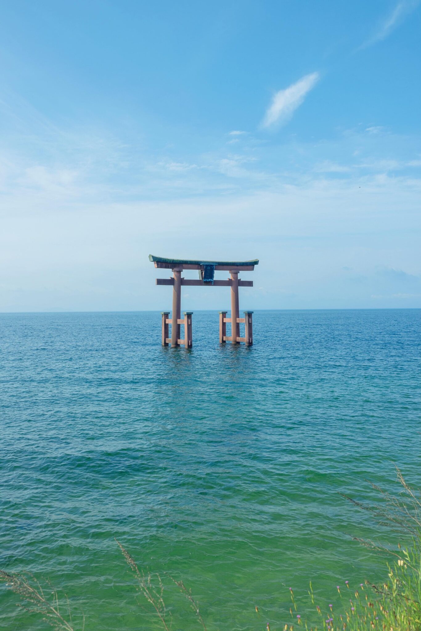 滋賀・奥琵琶湖で聖なる水辺を歩く旅。前編 | 近江最古の大社『白鬚神社』の湖中大鳥居。創建2000年余。『白鬚神社』（高島市鵜川215）は延命長寿のほか、縁結びや子授け、福徳開運、攘災招福、商売繁盛、交通安全など、人の世のあらゆる導きおよび道開きの神として信仰されてきた。湖中大鳥居は古より波打ち際に見え隠れしていた、また天下異変の前兆に突如姿を現したといった伝説が残り、室町時代の屏風絵にも描かれている。実際に鳥居が建立されたのは1937年、現鳥居は1981年に建て替えられたもの。