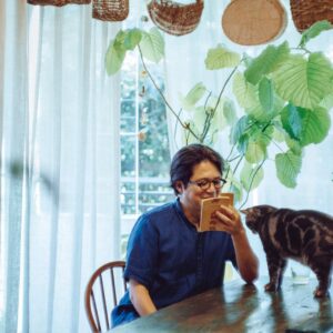 夜の古書店で、未知の本と出合う。歌人・穂村 弘さんの暮らしの本棚と、読書の時間の見つけ方。 | 自宅のリビングで読書をする穂村弘さん。愛猫のひるねがその姿を見つめる。 夜の古書店で、未知の本と出合う。歌人・穂村 弘さんの暮らしの本棚と、読書の時間の見つけ方。 | 自宅のリビングで読書をする穂村弘さん。愛猫のひるねがその姿を見つめる。