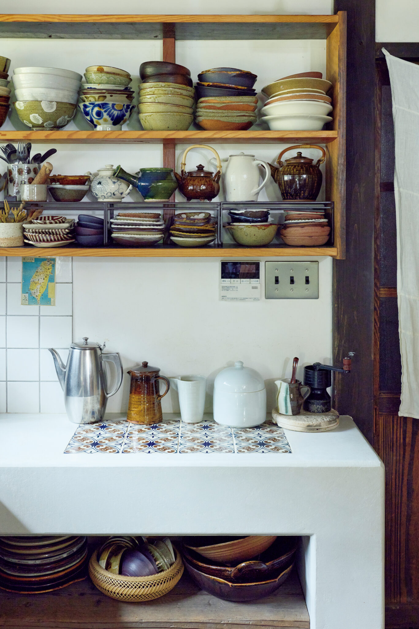 築150年のお勝手を、朗らかな台所に。古民家を改修した、心地よい台所。鳥取〈クラフト館 岩井窯〉の山本教行ら親交の深い窯元、作家の器が棚に並ぶ。モルタルの台には、〈瀬戸本業窯〉を訪ねた際に譲り受けた古い吉祥模様のタイルを埋め込んだ。ステンレスポットの隣は齊藤十郎のポット。「十郎さんからもらったミルをきっかけにハンドドリップが好きになりました」 | 鳥取〈クラフト館 岩井窯〉の山本教行ら親交の深い窯元、作家の器が棚に並ぶ。モルタルの台には、〈瀬戸本業窯〉を訪ねた際に譲り受けた古い吉祥模様のタイルを埋め込んだ。ステンレスポットの隣は齊藤十郎のポット。「十郎さんからもらったミルをきっかけにハンドドリップが好きになりました」　