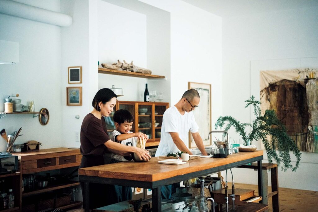 どの角度から眺めても、愛せる場所。自然と家族の真ん中にある、台所。 | 家族3人が横並びになって調理や作業ができる広々としたレイアウト。あかねさんと息子のむぎくんはパスタのお供にするシナモンロールづくりに没頭。