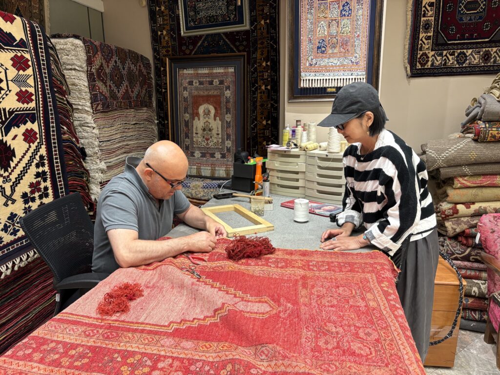 スタイリスト・石井佳苗さんと平井かずみさんが教えてくれた、ラグの楽しみ。 | 修復師が目の前で直している様子を眺める石井さん。「修復師はフリーで活動している人や店に所属の人もいるそうです」