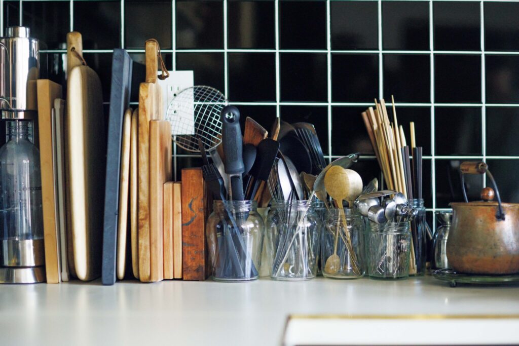 築50年の台所を改修したコックピット。料理家・小堀紀代美さんの台所。 | スプーンや菜箸、ターナーなどの調理道具の収納には空き瓶を活用。まな板はブックスタンドを使って立てて並べ、取り出しやすいようにしている。