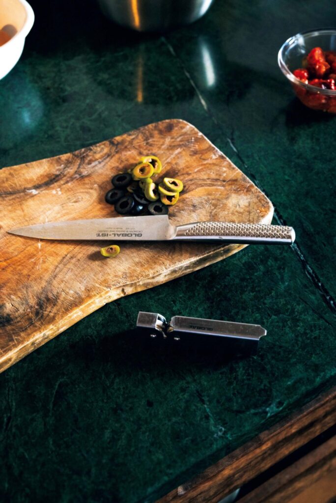 周囲の自然に溶け込む、部材の色に。菓子研究家・長田佳子さんの台所。 | カッティングボードは、オリーブの木の素材を愛用。包丁へのあたりが優しい。「〈グローバル〉の包丁はフィット感が抜群。専用のコンパクトなシャープナーを使えば、簡単に手入れできます」と長田さん。