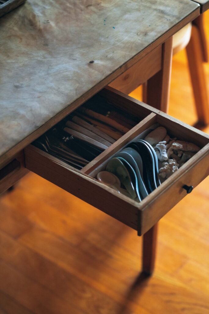 周囲の自然に溶け込む、部材の色に。菓子研究家・長田佳子さんの台所。 | ダイニングテーブルは小さな引き出し付きのものを選んだ。食事の準備がしやすいようにカトラリー類をまとめた。