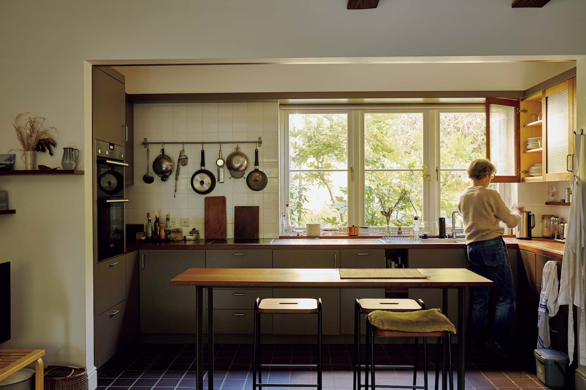 145_p078-085_マーガレット・ハウエル_01 | シンプルで洗練された空間が広がるマーガレット・ハウエルのキッチン。左側の壁に吊るした調理道具は毎日使うもの。手前のダイニングテーブルで食事をすることが多い。 145_p078-085_マーガレット・ハウエル_01 | シンプルで洗練された空間が広がるマーガレット・ハウエルのキッチン。左側の壁に吊るした調理道具は毎日使うもの。手前のダイニングテーブルで食事をすることが多い。