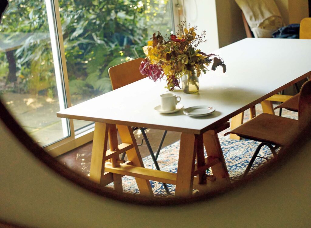 145_p078-085_マーガレット・ハウエル_17 | 普段食事をするのは一枚目の写真にあるハイテーブルだが、家族や友人らが集まった際には、窓際にある大きなダイニングテーブルを囲む。壁一面が窓で美しい庭の緑が望める。