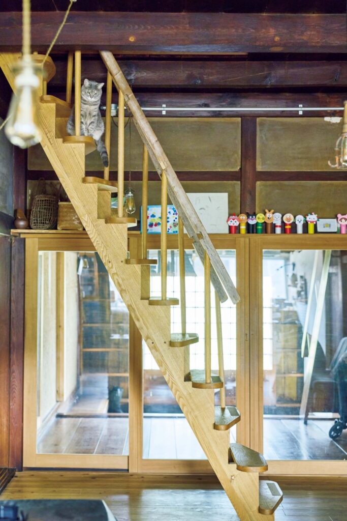 弧を描く白壁を、古民家暮らしの象徴に。〈JAPONISME〉運営の白石さん夫妻が住む築70年の家。 | 階段の先は家族の寝室。薪ストーブの煙突を通じて、寒い冬もぬくぬくで過ごせる。木の階段は愛猫・すずのお気に入り。