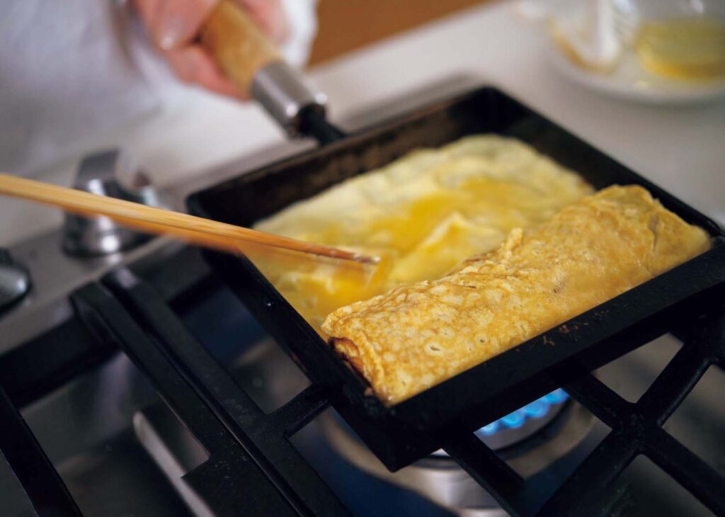 &CookingM_p006-053_献立編_04_絵柄のばし | 玉子焼きの下に菜箸を入れて持ち上げ、卵液をすみずみまで流し入れてよく焼く。 &CookingM_p006-053_献立編_04_絵柄のばし | 玉子焼きの下に菜箸を入れて持ち上げ、卵液をすみずみまで流し入れてよく焼く。