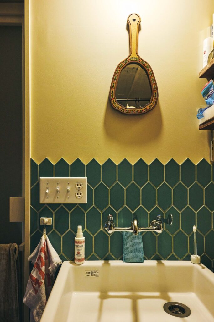 自分史を詰め込むための古くて大きな部屋。卯月えまさんが住む築55年の家。 | 家事室と呼んでいる空間にクローゼット、洗濯機と並んで洗面所が。緑のタイルは日本製。手鏡は〈HYST〉で。