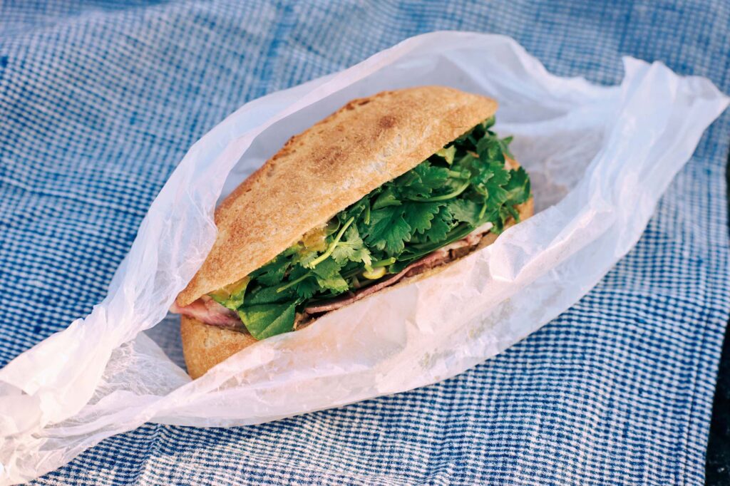 人を引き寄せる、ゆるやかな水辺のリズム。京都・鴨川、ローカルガイド。後編 | 『120グラムバインミー京都』（左京区聖護院東寺領町6‒2）のクラシックバインミー（￥1,200）は鴨川べりがよく似合う。「パリパリもっちりな自家製バゲットに季節の野菜がたっぷり入り、ボリューム満点なのにあっという間にぺろり」