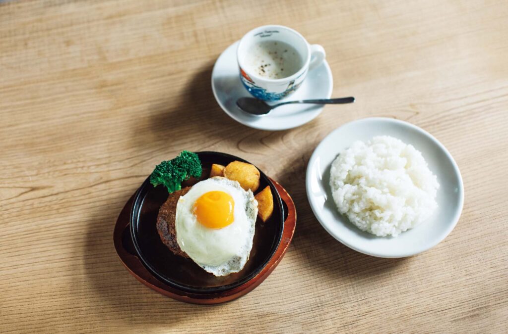 人を引き寄せる、ゆるやかな水辺のリズム。京都・鴨川、ローカルガイド。後編 | 2025年11月に旧店舗のほぼ向かいに移転リニューアルした『イノツチ洋食店』（左京区頭町337‒79）。看板メニューの鉄板ハンバーグ（目玉焼きトッピングで￥1,700）は季節野菜のポタージュ付き。寺の境内に位置し、風雅な庭が望める。