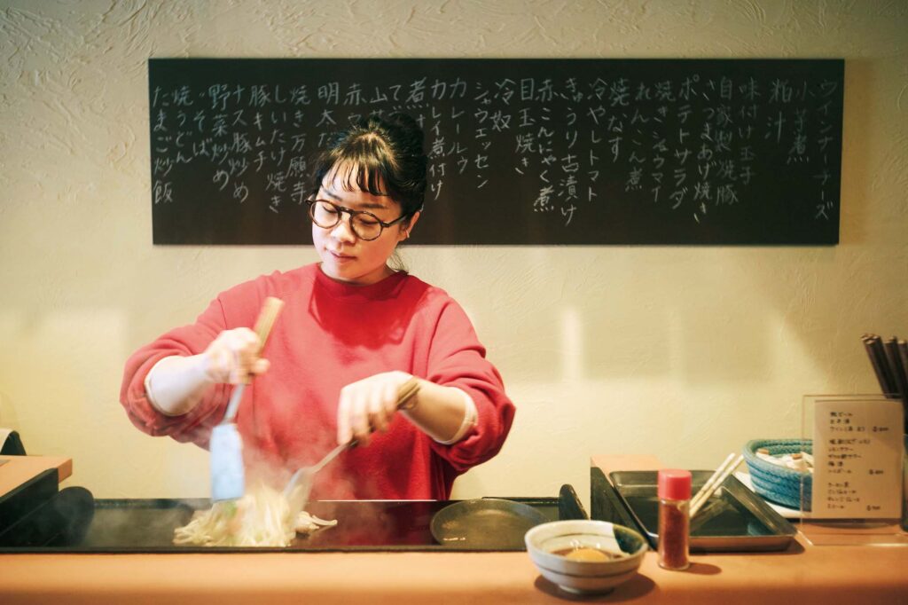 人を引き寄せる、ゆるやかな水辺のリズム。京都・鴨川、ローカルガイド。後編 | 「店主のなおさんの安定感ある接客と鉄板さばきで、カウンターながらくつろいで飲んでしまいます」という居酒屋『とよこや』（中京区清水町352‒4）。野菜炒め（￥900）にポン酢と生卵（￥100）をつけて食べるのが酒向さんのお気に入り。