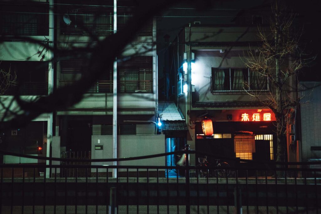 人を引き寄せる、ゆるやかな水辺のリズム。京都・鴨川、ローカルガイド。後編 | 戦前から縄のれんを守る名店『赤垣屋』（左京区孫橋町9 ）。店名のネオンと赤提灯はすっかりエリアのランドマークに。開店の午後5 時前には列ができるが、遅い時間に覗いて入店のチャンスをうかがうのが常連の日常とか。