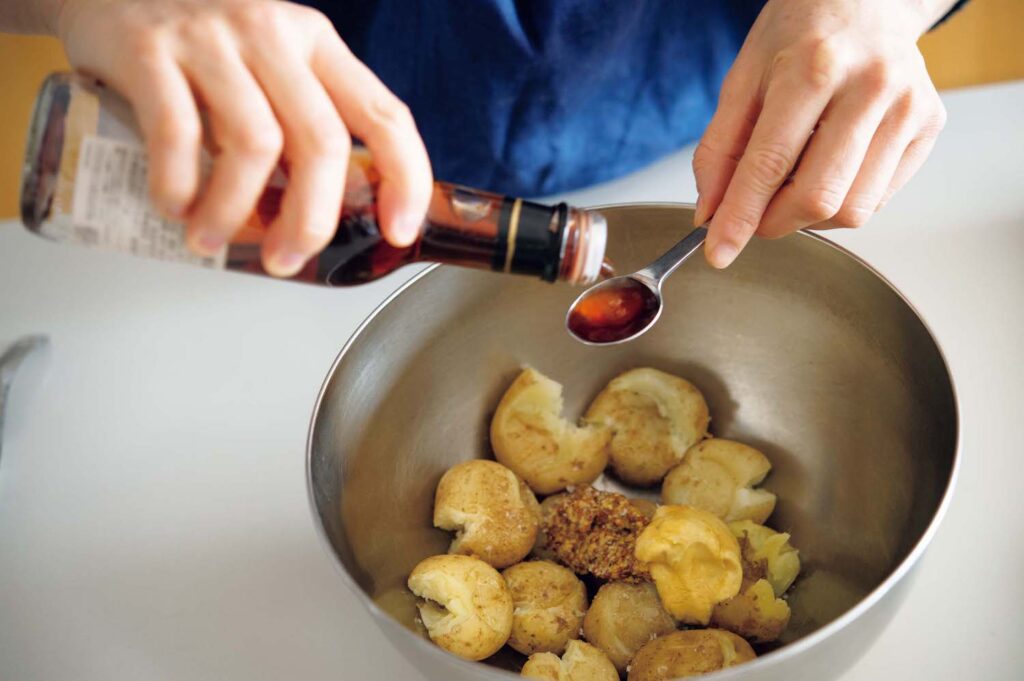 春野菜とハーブの洋食。渡辺有子の料理教室3年目3月。蒸した小ジャガイモは木ベラで軽く潰し、熱いうちに調味料を加えて和える。 | 蒸した小ジャガイモは木ベラで軽く潰し、熱いうちに調味料を加えて和える。