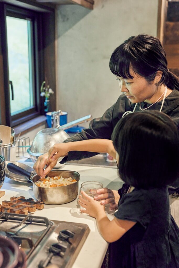 森をのぞむ台所。移ろう景色が家事の支えに。鍋に野菜を重ねて入れたら、咲那ちゃんも一緒に仕上げの塩をぱらり。 | 鍋に野菜を重ねて入れたら、咲那ちゃんも一緒に仕上げの塩をぱらり。 森をのぞむ台所。移ろう景色が家事の支えに。鍋に野菜を重ねて入れたら、咲那ちゃんも一緒に仕上げの塩をぱらり。 | 鍋に野菜を重ねて入れたら、咲那ちゃんも一緒に仕上げの塩をぱらり。