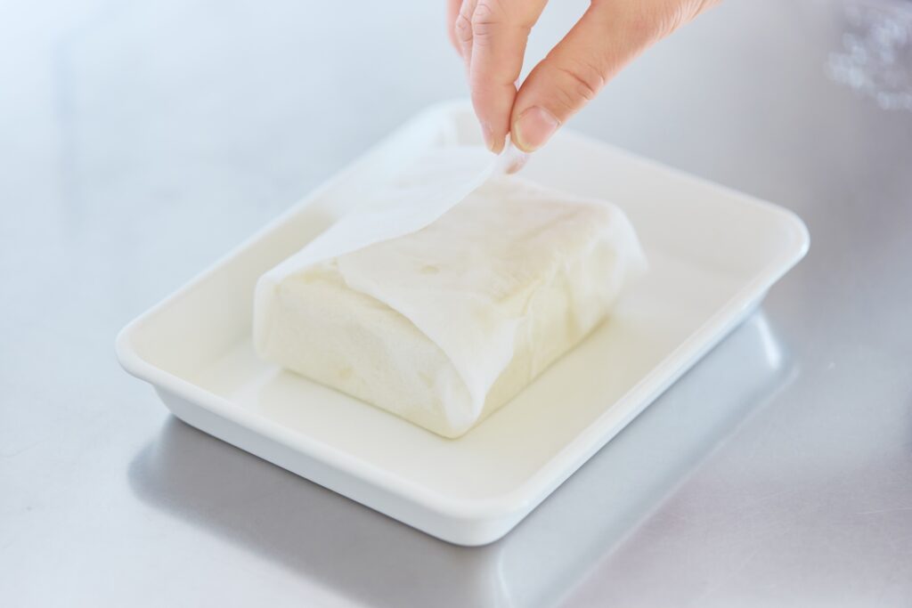 〈POINT〉豆腐を「リード クッキングペーパー」で包んで、半日以上水切りをする。吸収力が高いので、重しを乗せなくてもOK。余分な水分を落とすと、調味がしやすくなる。 | 〈POINT〉豆腐を「リード クッキングペーパー」で包んで、半日以上水切りをする。吸収力が高いので、重しをのせなくてもOK。余分な水分を落とすと、調味がしやすくなる。