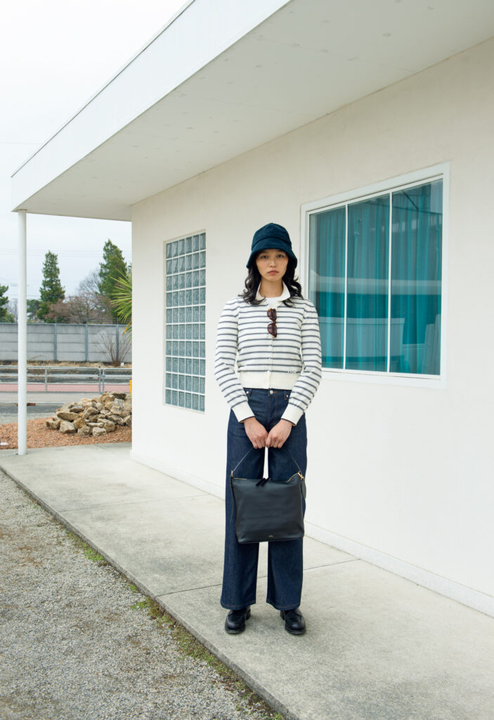 ブラックのグレインレザーのボディに、ゴールドの金具が映える上品な佇まいの「Vera」。裏地付きの丁寧な仕立てに、大きなダブルファスナーで荷物の出し入れもスムーズ。ミニマルな造形の中に機能と美が調和する。バッグ￥104,500、チャーム￥14,300、カーディガン￥50,600、Ｔシャツ￥15,400、デニムパンツ￥33,000、ハット￥22,000、サングラス￥42,900 (以上A.P.C.／アー・ペー・セー カスタマーサービス) 