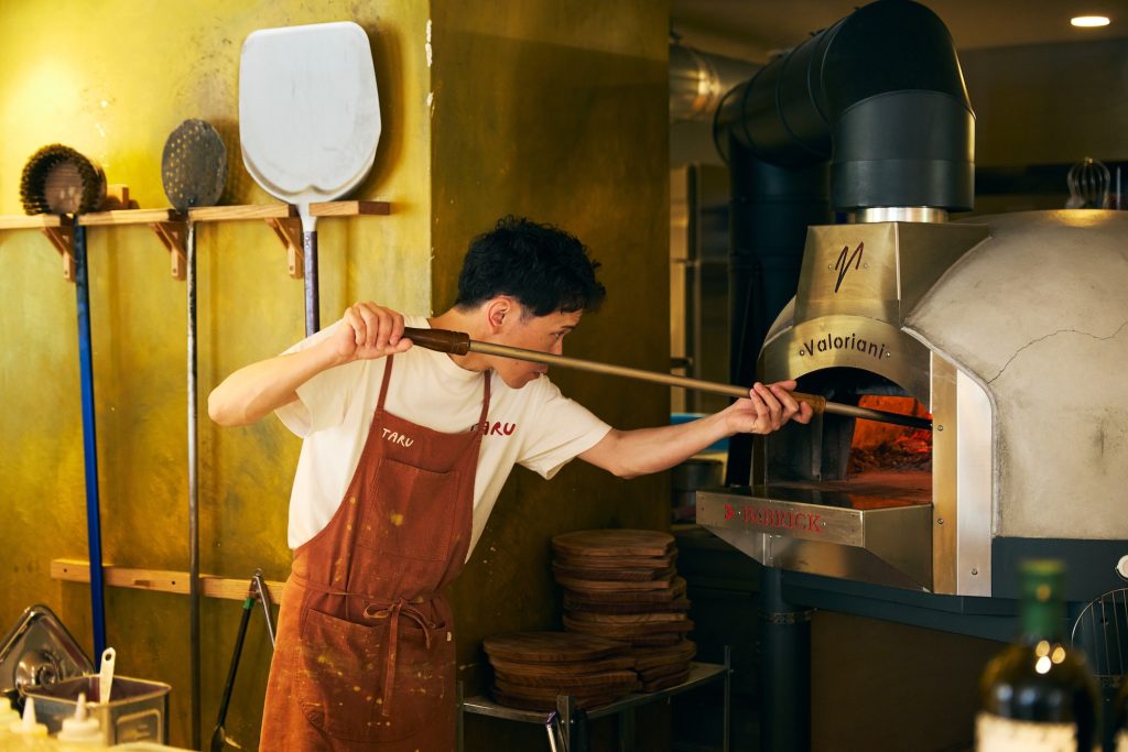 『TARU』のオープンキッチンにはイタリア製の薪窯があり、目の前でピザを焼きあげる姿を見ることができる。 | 『TARU』のオープンキッチンにはイタリア製の薪窯があり、目の前でピザを焼き上げる姿を見ることができる。