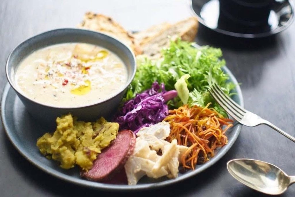お昼の「パンとスープと旬の野菜たっぷりプレート」¥1,650ほか。今日は新玉ねぎと新ジャガイモとズッキーニの豆乳ポタージュ、人参のバルサミコラペ、紫キャベツのキャラウェイマリネ、レンコンのビーガンバーニャカウダ、紅くるりのソテー、さつまいものサブジ。