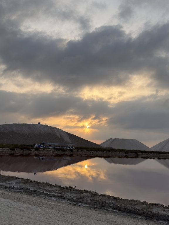 夕方になると、塩の山の向こうに沈む太陽が塩田の水面に映り込み、幻想的な風景が広がる。まるで砂丘のように見える山は、すべて地中海の海水から作られた粗塩でできており、ラクダのコブのように見えることから、現地では「キャメル」と呼ばれる。