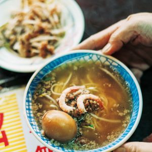 老若男女に愛される、地元ならではの味。台南フードを味わう。台南発祥の担仔麺（タンツァイミエン）小60元。すりおろし生ニンニク、パクチー、エビなどをトッピング。「栄養たっぷりな煮卵（15元）も欠かせません」と案内人で『蘿拉冷飲店 LOLA』オーナーのジンジンさん。 | 台南発祥の担仔麺（タンツァイミエン）小60元。すりおろし生ニンニク、パクチー、エビなどをトッピング。「栄養たっぷりな煮卵（15元）も欠かせません」と案内人で『蘿拉冷飲店 LOLA』オーナーのジンジンさん。