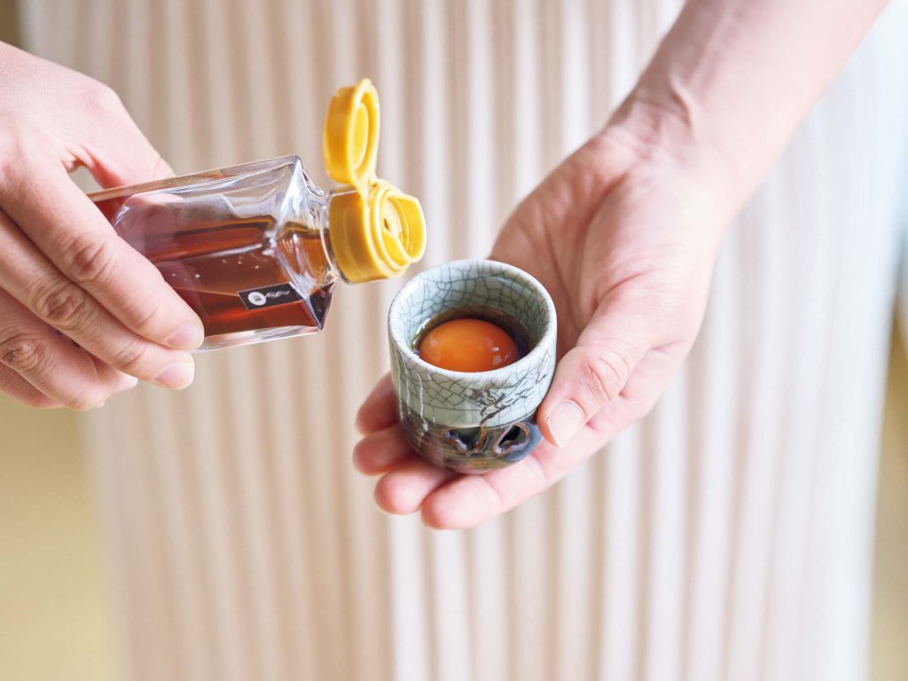 黄身をだし醤油に漬ける様子 | 黄身をだし醤油に漬けるのにはムダの出ない小さなおちょこが向く。黄身を取り出した後は〝追い醤油〞に使う。