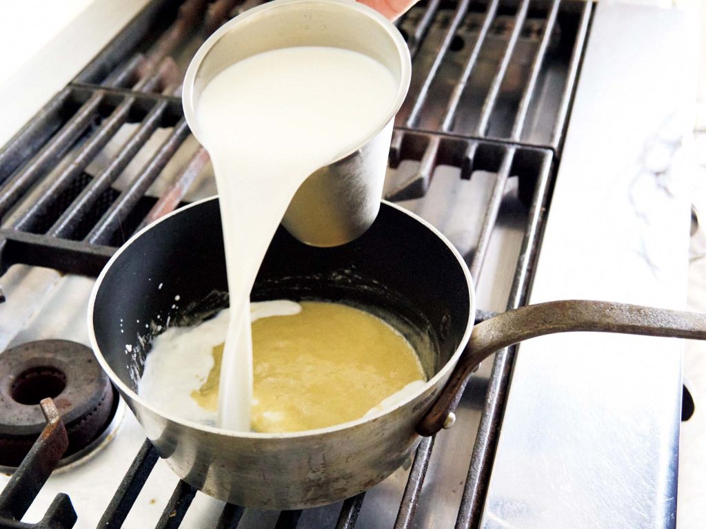 本気のグラタンを作る。ソースも具もひと手間かけて。 湯気まで味わう、ごちそう。鍋を火から外し、牛乳を2回に分けて注いだら、泡立て器で軽く混ぜ、弱めの中火にかけて木ベラで混ぜながら煮詰める。 | 鍋を火から外し、牛乳を2回に分けて注いだら、泡立て器で軽く混ぜ、弱めの中火にかけて木ベラで混ぜながら煮詰める。