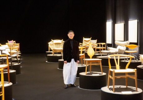 「織田コレクション ハンス・ウェグナー展 至高のクラフツマンシップ」の会場で、自身も愛用するバレットチェアの隣に立つ〈ミナ ペルホネン〉デザイナーの皆川 明さん。会場構成は建築家・田根剛が担当。 | 「織田コレクション　ハンス・ウェグナー展　至高のクラフツマンシップ」の会場で、自身も愛用するバレットチェアの隣に立つ〈ミナ ペルホネン〉デザイナーの皆川 明さん。会場構成は建築家・田根剛が担当。